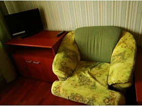 телевизор на тумбочке и мягкое кресло в зеленом цвете в комнате отдыха