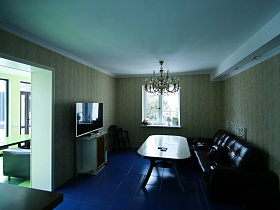 мягкая черная мебель у обеденного стола, кресло, телевизор на тумбе на полу с синей квадратной плиткой большого дома