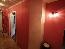бра на стене и мягкий круглый пуфик в углу прихожей в розово пастельных тонах семейной трешки
