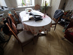 стулья со спинками вокруг круглого стола с белой скатертью, велосипед у окон гостиной квартиры сталинки
