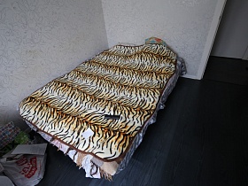 наполненные пакеты у большой кровати с тигровым покрывалом  на полу с темно серым линолеумом светлой спальной комнаты современной двухкомнатной квартиры
