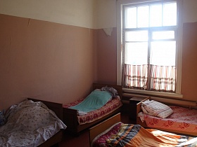 ряды деревянных кроватей с подушками на марселевом покрывале у стен, требующих ремонта палаты с пестрыми ситцевыми шторками на большом окне старой действующей больницы