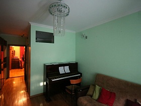 ноты на открытом пианино, стул со спинкой, мягкий диван с разноцветными подушками у голубой стены спальной комнаты стильной квартиры
