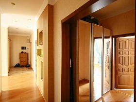 черный чемодан на верху шкафа-купе с зеркальными дверцами в небольшом коридоре с открытой дверью в спальную комнату современной трехкомнатной квартиры