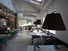 ровные ряды сервированных столиков с мягкими креслами и синими стульями с индивидуальным освещением в просторном зале ресторана с белыми стенами и белым деревянным потолком