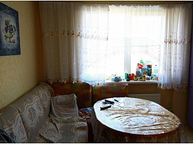 картина над мягким уголком с покрывалом у окна с короткой гардиной в кухне трешки панельного дома