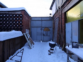 высокие металлические ворота с входной дверью на собственный двор под снегом музыкального стильного магазина электронных гитар в кирпичном здании