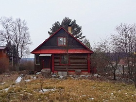 красная крыша над закрытой верандой и крыльцом у входной двери в деревянный дом на большом участке в деревне
